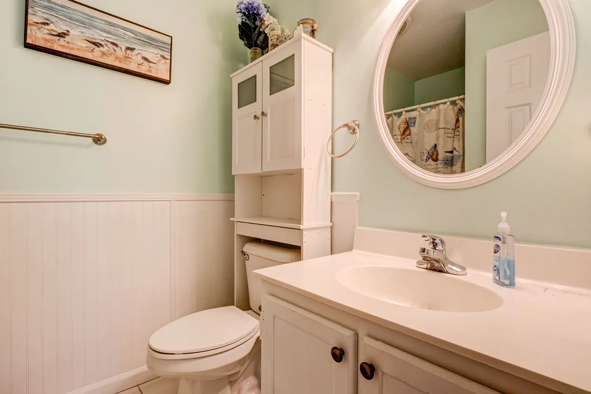 A serene and refreshing bathroom with a white vanity, round mirror, decorative wall art, a toilet, and a bathroom cabinet. Soft natural light creates a calming setting for morning and evening routines.