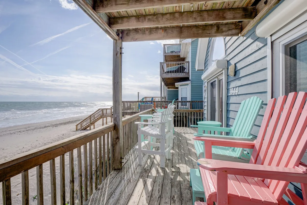 An exterior deck furnished with colorful Adirondack chairs overlooking the ocean, with a sturdy railing defining the space. The deck invites outdoor relaxation, sunset viewing, and easy transition from inside to out.