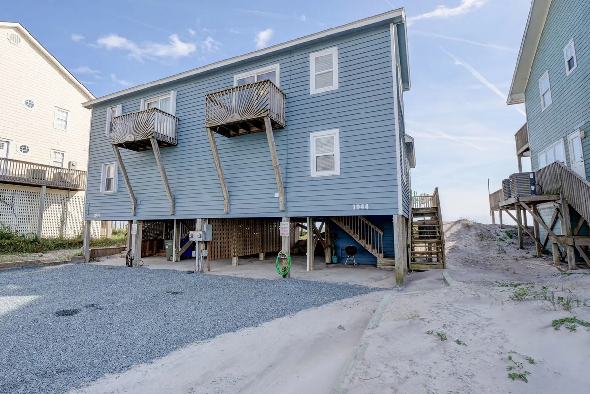 A bright view of the blue exterior with multiple balconies and a shaded porch area underneath. Visible parking and open spaces emphasize convenience for groups and opportunities for outdoor gatherings, morning coffee, or evening barbecues.